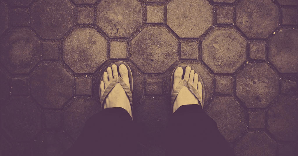 Top view of feet in flip-flops on a tiled surface, symbolizing how to check your arches for flat feet